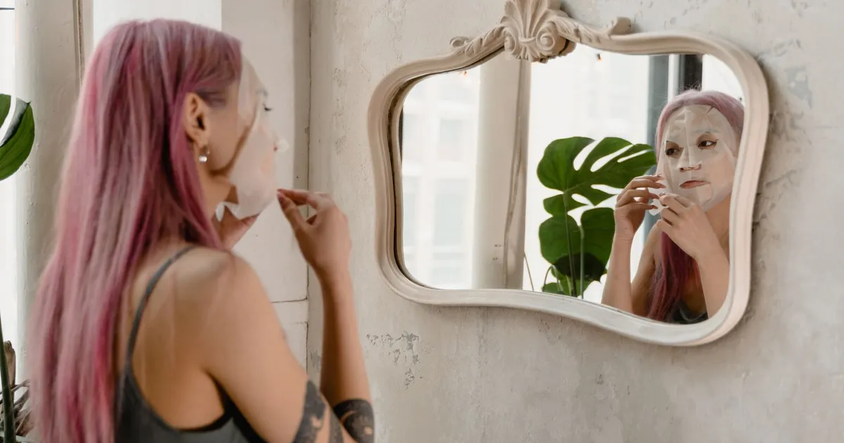A woman applying a facial mask in front of a mirror