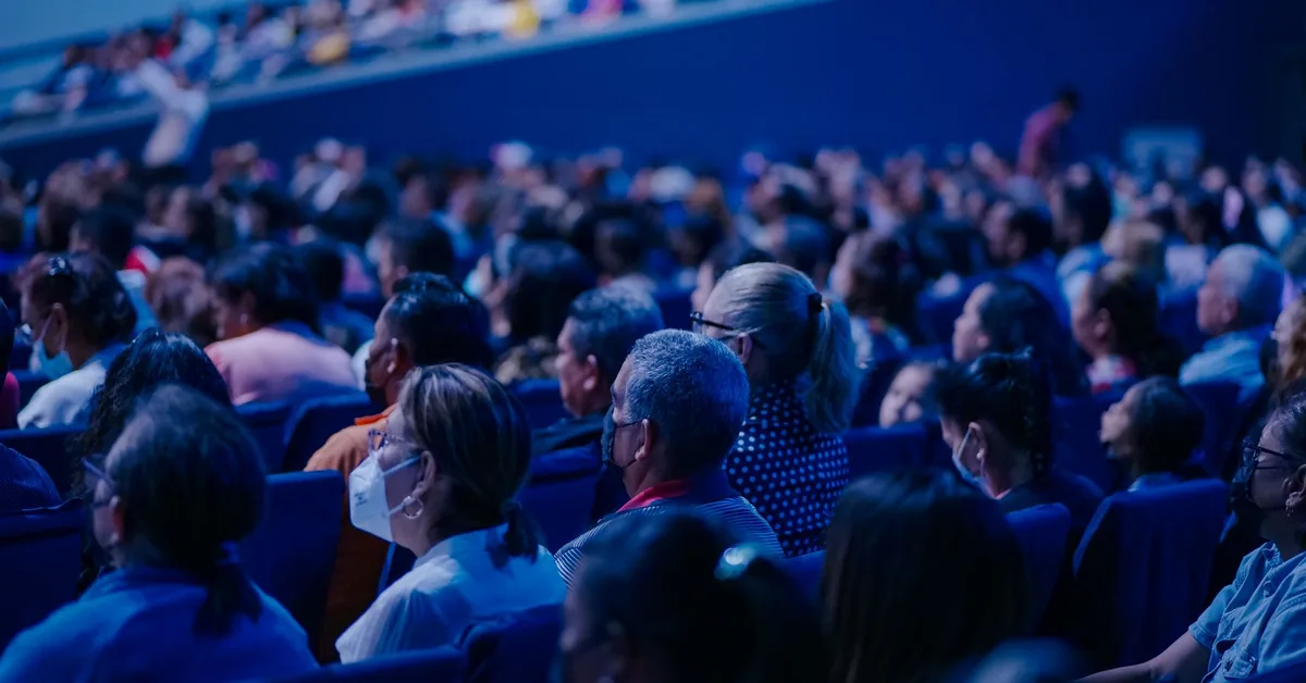An audience seated in a conference auditorium under blue lighting