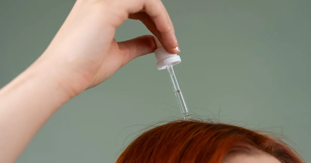 A dropper applying serum to red hair