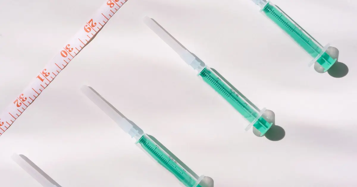 Green-filled syringes and a measuring tape on a white surface