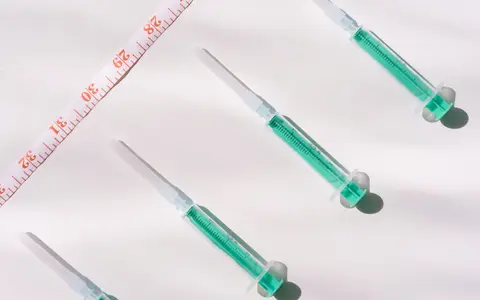 Green-filled syringes and a measuring tape on a white surface