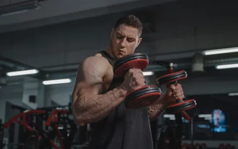 A man curling a dumbbell during a workout in a gym
