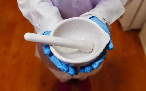 A pharmacist in blue gloves and a lab coat holding a white mortar and pestle