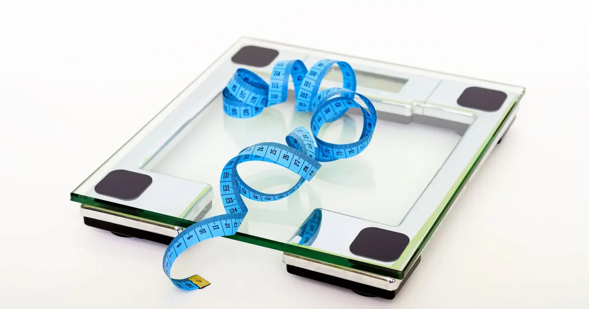 A digital glass bathroom scale with a blue tape measure resting on it
