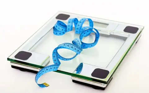 A digital glass bathroom scale with a blue tape measure resting on it
