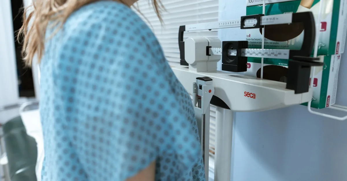 A clothed patient standing at a medical weighing and measurement station