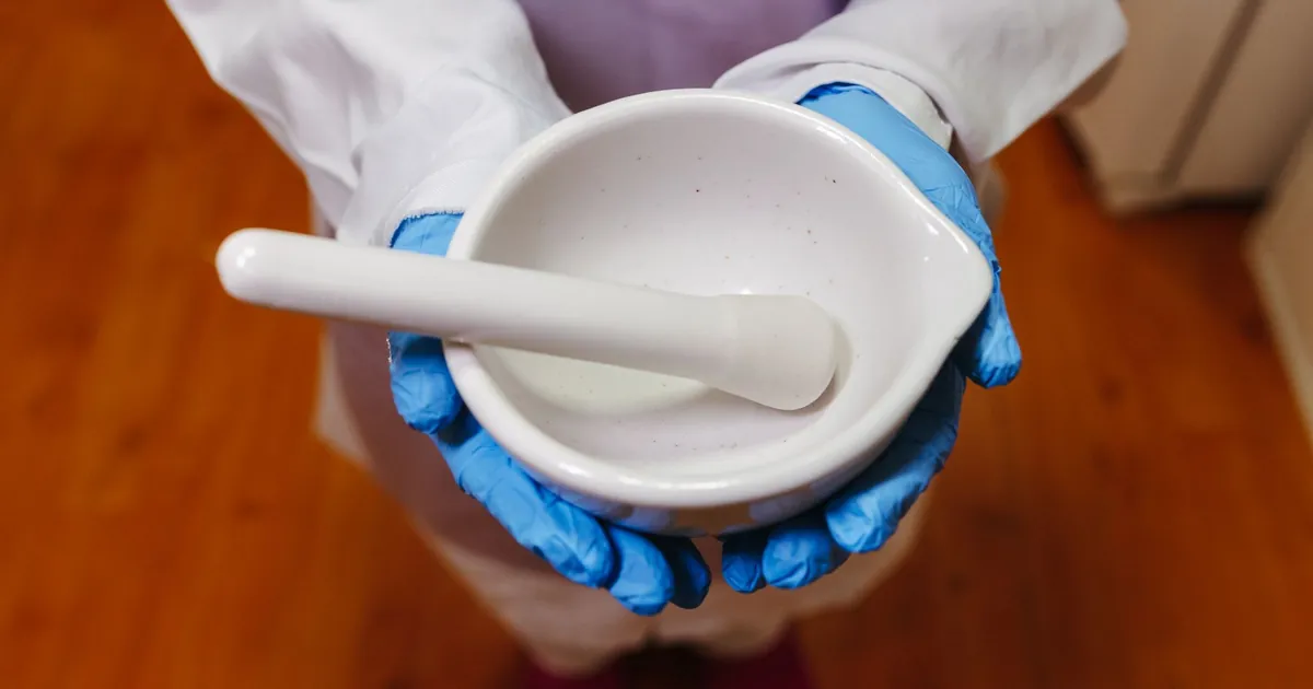 Gloved hands holding a white mortar and pestle