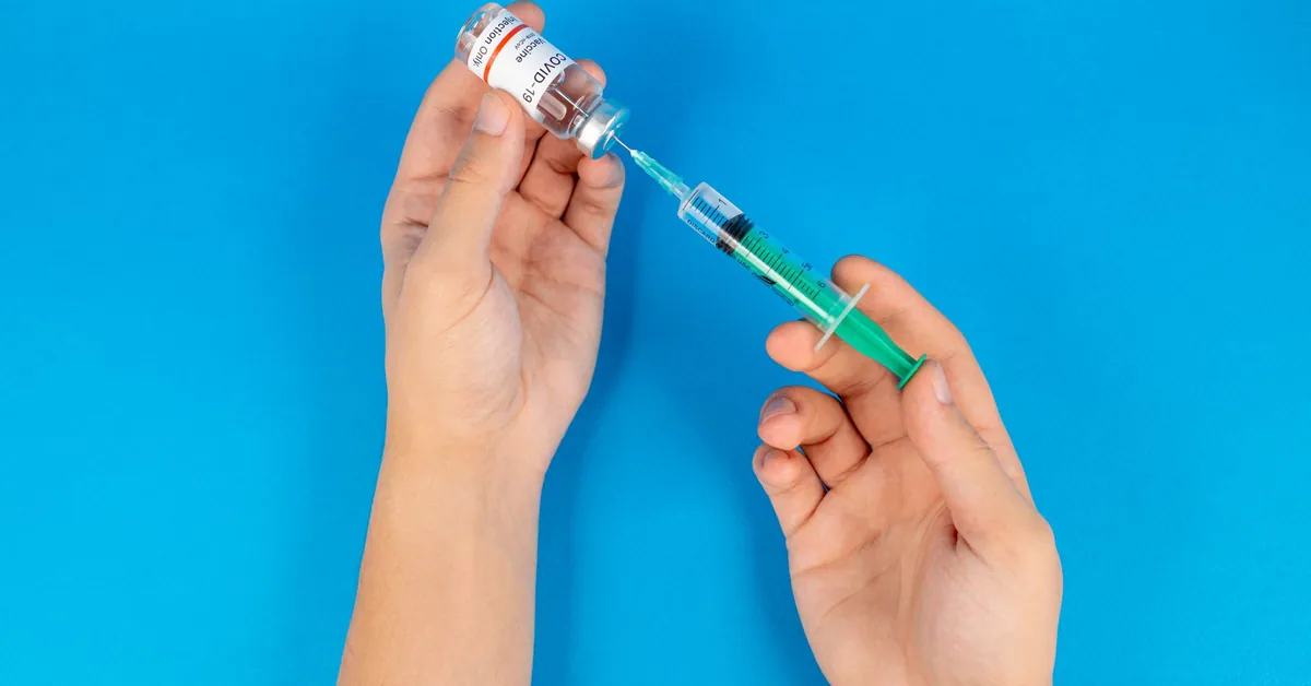 Gloved hands drawing liquid from a vial into a syringe