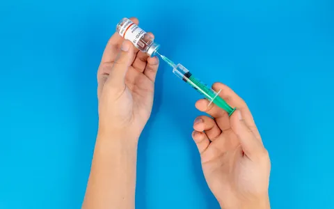 Gloved hands drawing liquid from a vial into a syringe