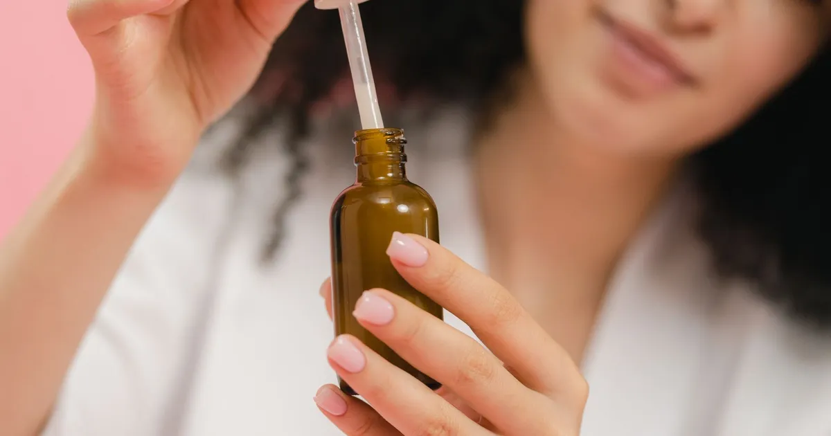 A woman holding a brown glass dropper bottle of skin serum