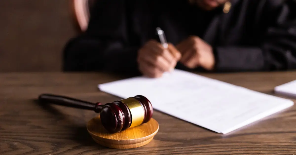 A judge signing documents at a desk, with a gavel in the foreground