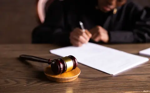 A judge signing documents at a desk, with a gavel in the foreground
