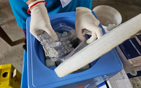 A gloved healthcare worker handling medical vials in a laboratory