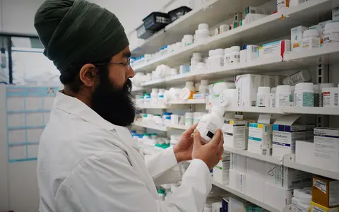 Pharmacist with turban organizing shelves in a pharmacy, focused on healthcare