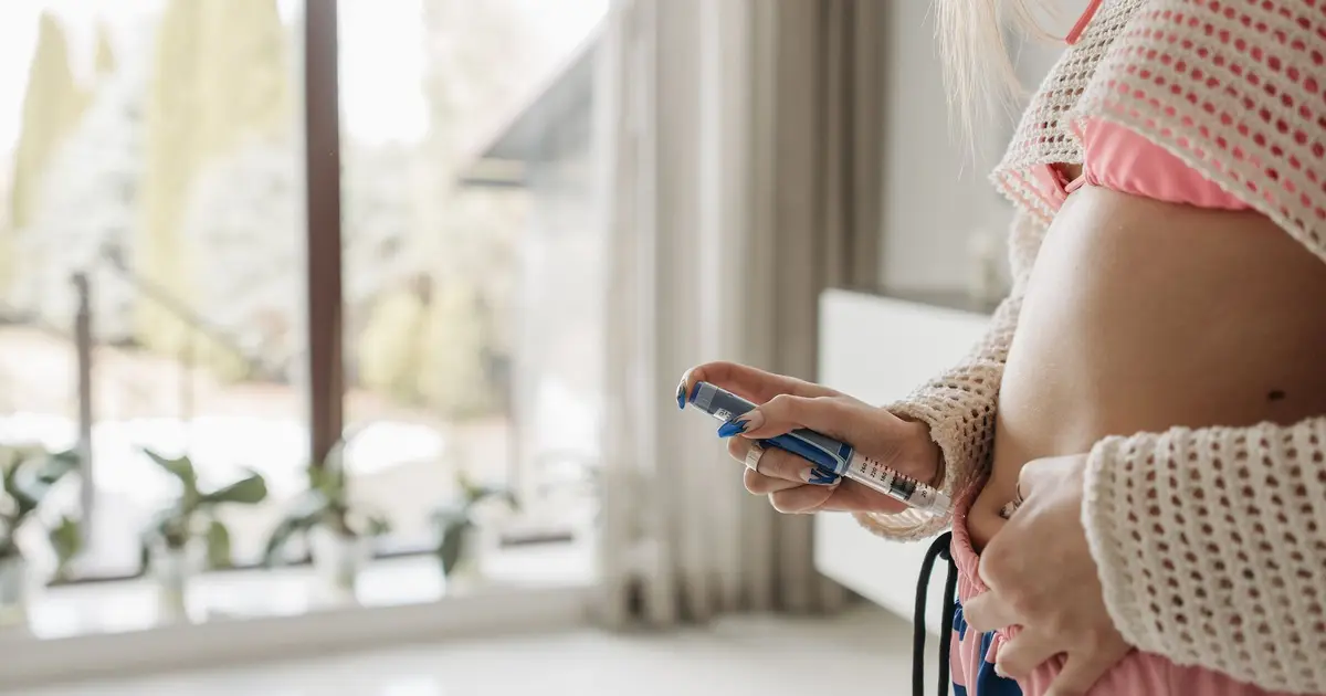 A woman holding a pen injector to her abdomen for an injection at home