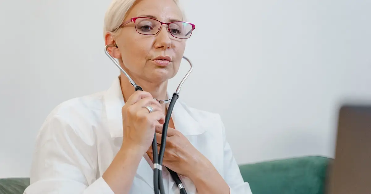 Elderly female doctor using a stethoscope during a virtual consultation in a medical office