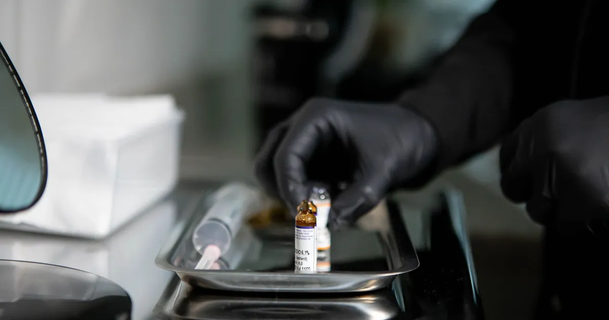 Gloved hands arranging medicine vials on a stainless steel tray