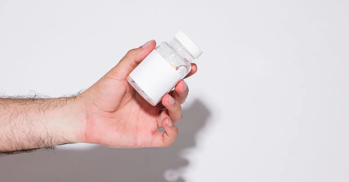 A hand holding a small white pill bottle