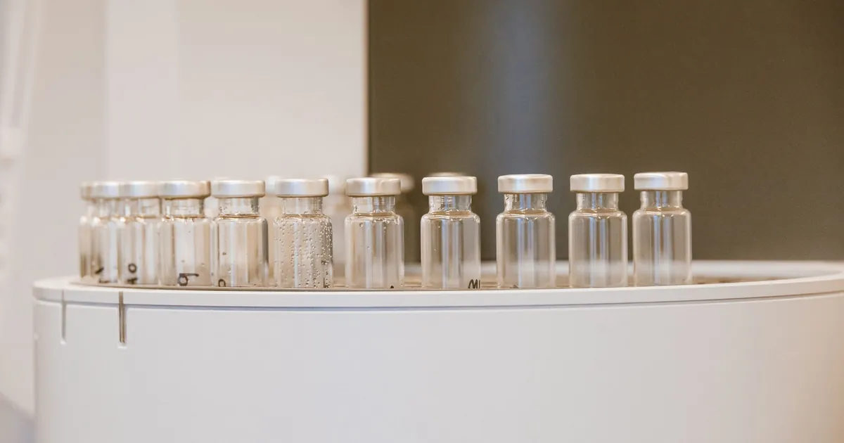 A row of small clear glass vials with metal caps on a white tray, a few marked by hand