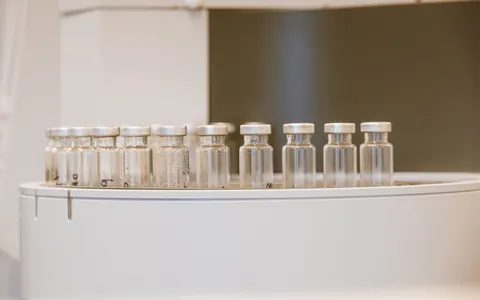 A row of small clear glass vials with metal caps on a white tray, a few marked by hand