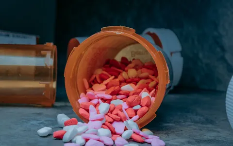 An overturned prescription bottle with capsules spilling onto a surface
