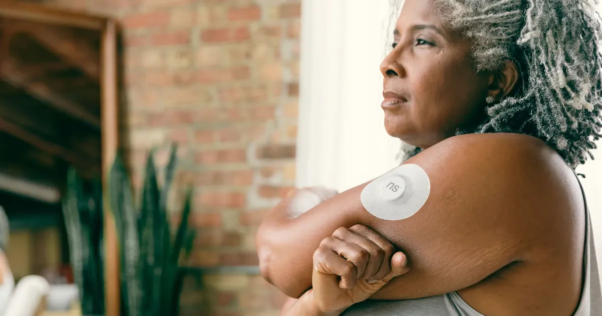 A woman wearing a continuous glucose monitor on her arm