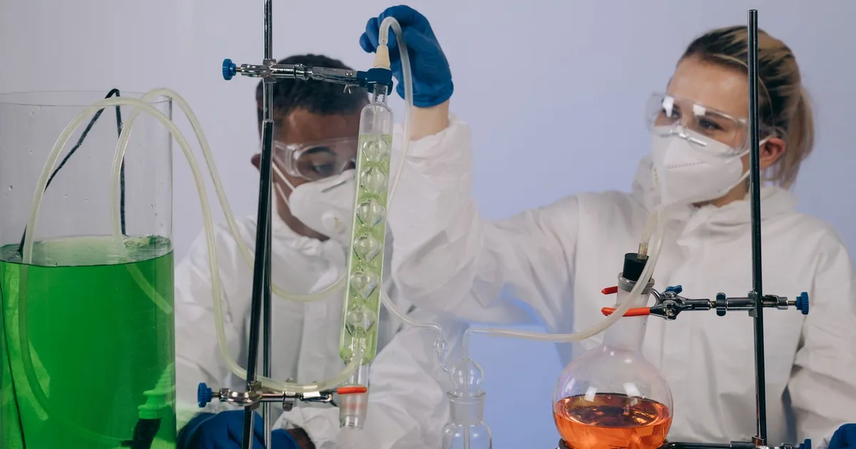 Chemists in protective gear performing an experiment in a laboratory
