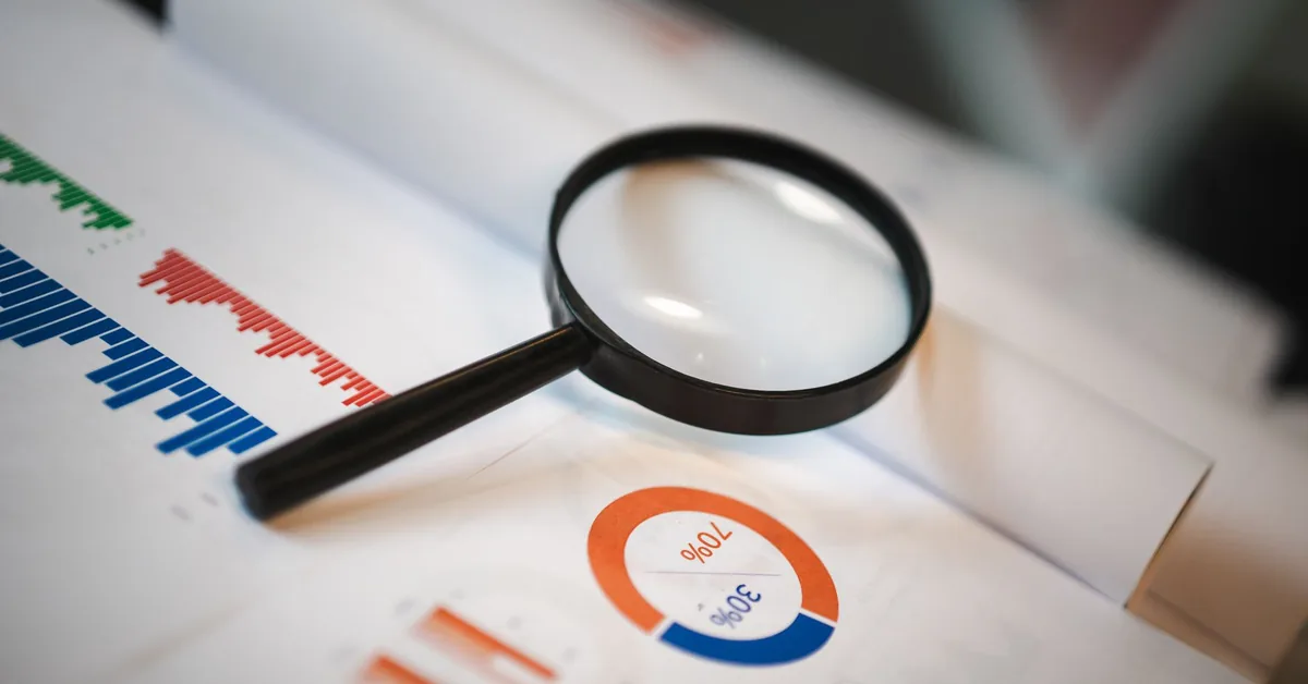 A magnifying glass held over printed documents and charts