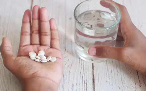 A close-up of hands holding medication tablets and a glass of water on a wooden surface