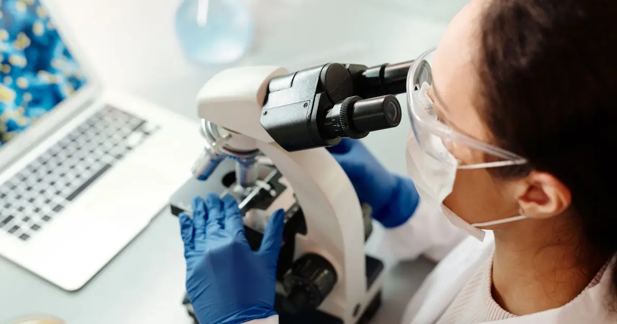 Scientist in protective gear examining samples with microscope in laboratory setting
