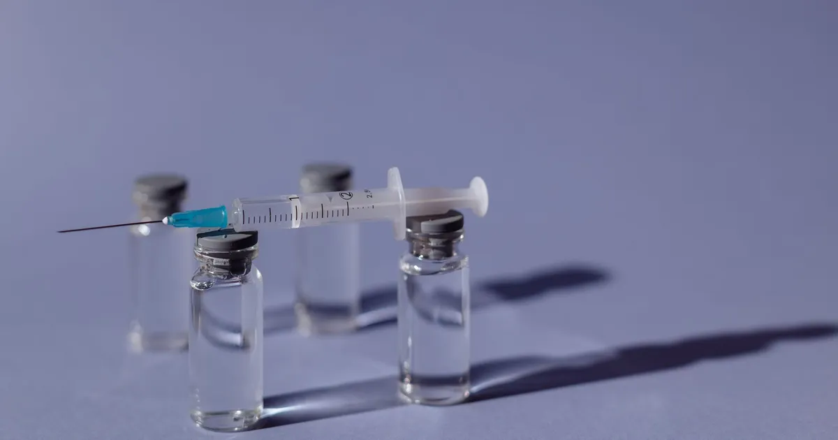 A syringe resting on medicine vials against a purple background