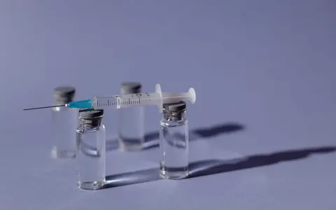 A syringe resting on medicine vials against a purple background