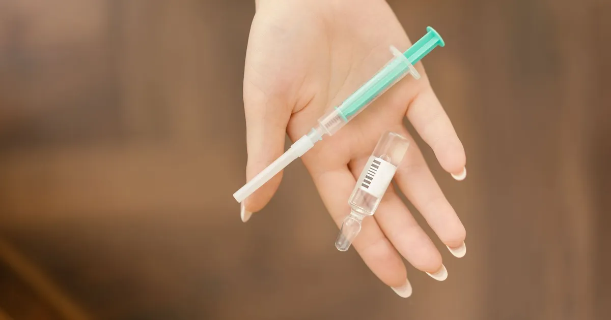 A gloved hand holding a syringe and a small glass vial