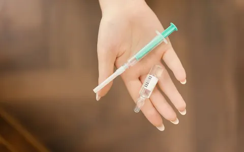 A gloved hand holding a syringe and a small glass vial