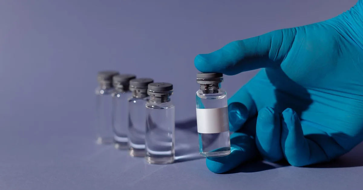 A gloved hand holding a clear medical vial against a blue background