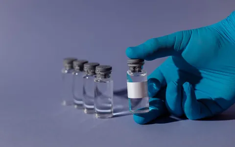 A gloved hand holding a clear medical vial against a blue background