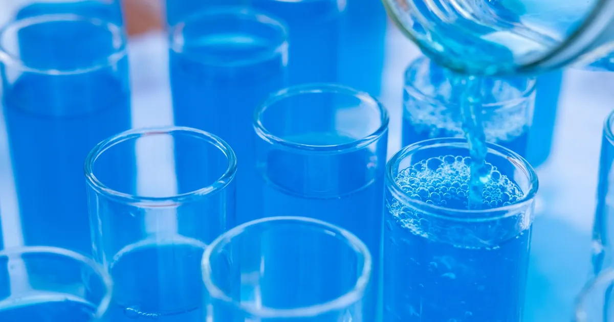 Blue liquid being poured from a beaker into rows of clear glass tubes