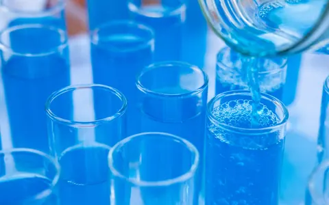 Blue liquid being poured from a beaker into rows of clear glass tubes