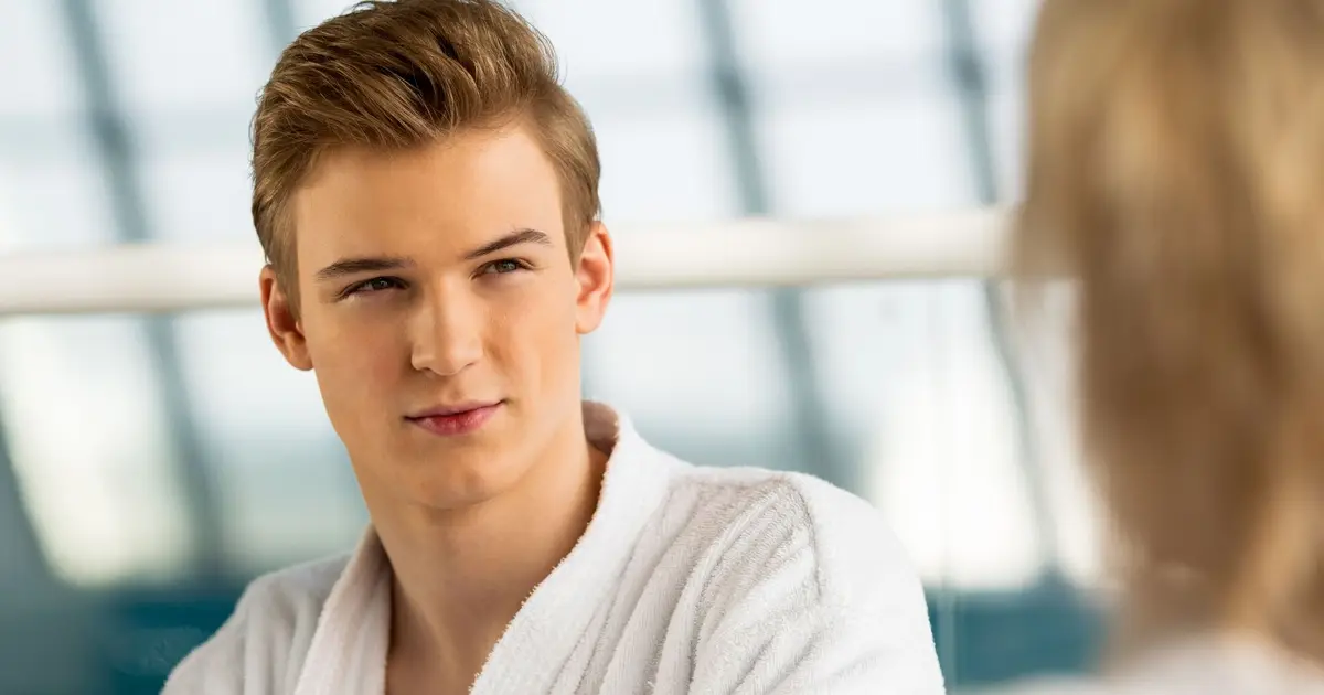 Portrait of an attractive young man in a bathrobe, looking into the distance by a large window