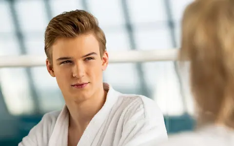 Portrait of an attractive young man in a bathrobe, looking into the distance by a large window