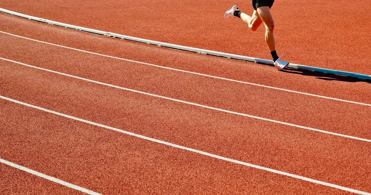 Athlete running on a red track in an outdoor stadium on a sunny day