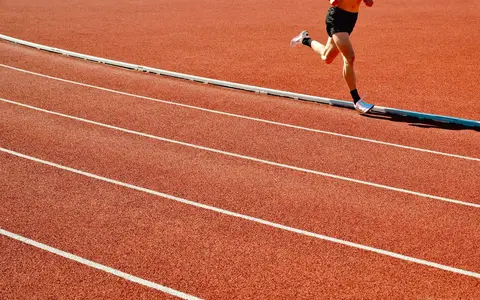 Athlete running on a red track in an outdoor stadium on a sunny day