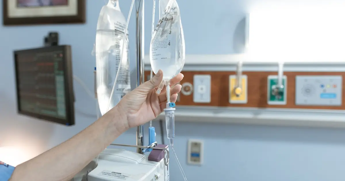Close-up image of an IV drip and hand in a hospital room, illustrating medical care