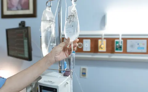 Close-up image of an IV drip and hand in a hospital room, illustrating medical care
