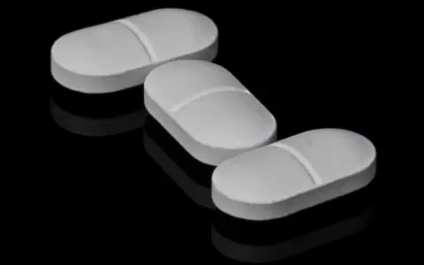 Three white tablets on a dark reflective surface