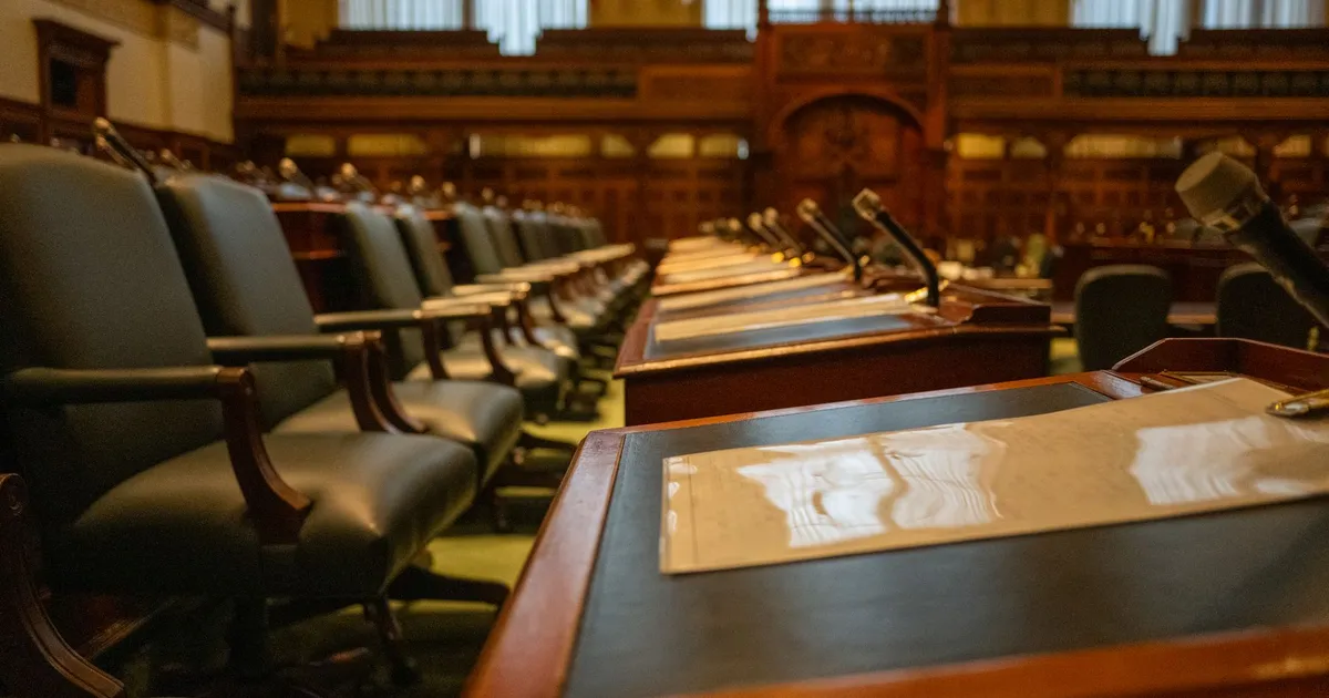 An empty legislative chamber with rows of desks and microphones
