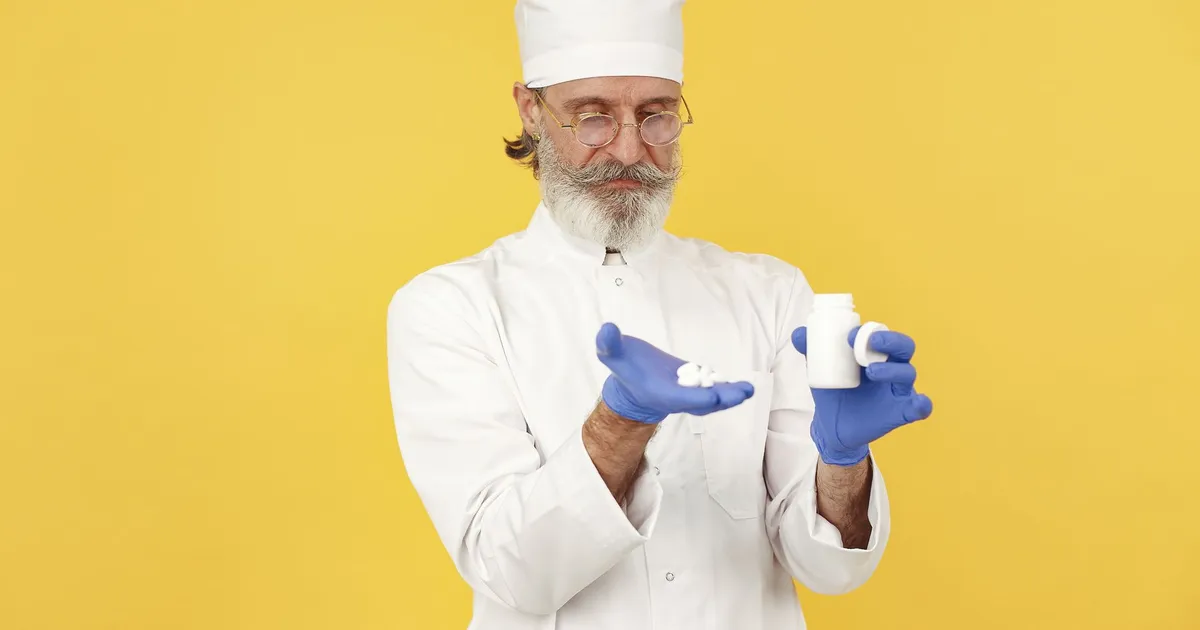 A pharmacist examining tablets in his palm beside a medicine bottle