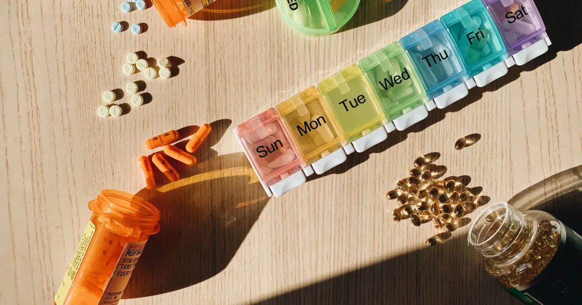 A colourful pill organizer with medication bottles on a wooden table