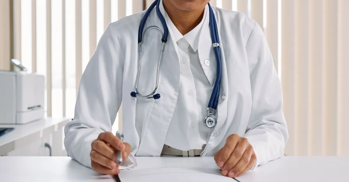 A doctor in a white coat writing notes at a desk