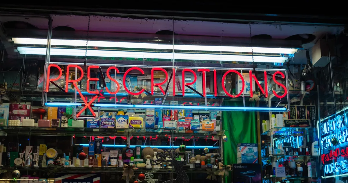 An illuminated pharmacy sign advertising prescriptions above a storefront at night